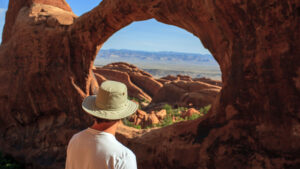 A man looks through the red rock arches in Moab - Moab Giants